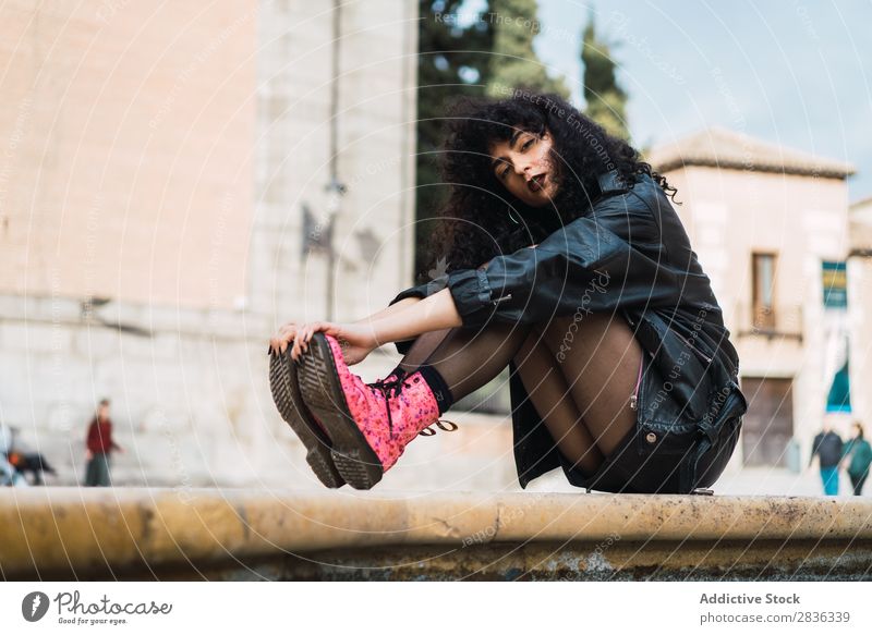 Young woman posing at fountain Woman Attractive City fashionable Curly Brunette Jacket Fountain Water Looking into the camera Fashion Youth (Young adults)