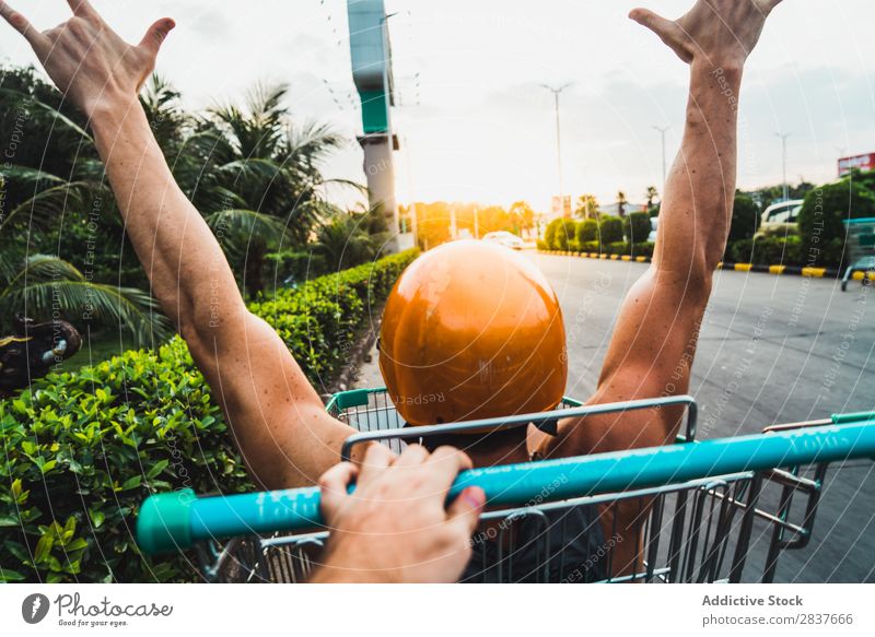 Man riding in shopping cart Shopping Trolley Cart pushcart shopper Ride handsome Cheerful Joy Parking lot Human being Pushing Markets Humor Carriage Happy