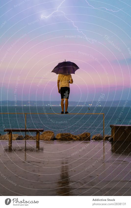 Jumping man with umbrella in nature Man Umbrella Posture Acrobat Expression Embankment Rain Movement gymnastic above ground Ocean Performance Athletic