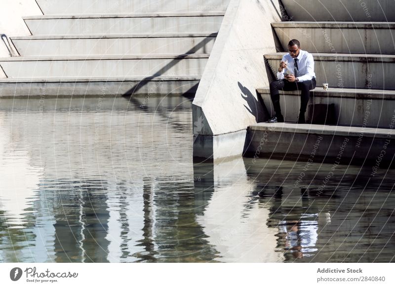 Elegant young man sitting on stairs drinking coffee and eating snack. male successful stylish beverage confidence breakfast businessman morning manager african