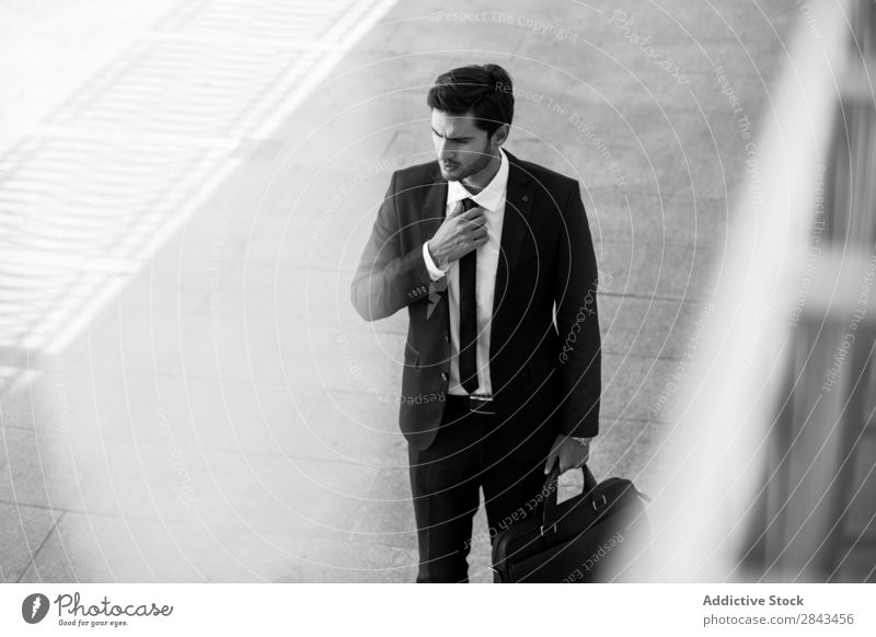 Serious businessman with briefcase holding hand on tie Businessman Street black & white Earnest Portrait photograph Looking away Hold Hand Tie Pensive Stand