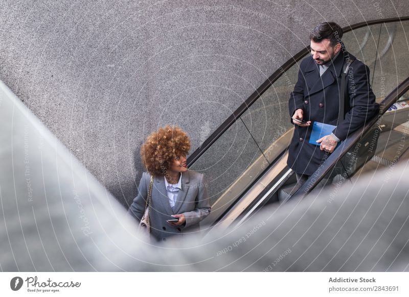 Stylish couple with phone on escalator Couple Adults Style Beautiful Escalator moving stairs PDA using Coat warm clothes Together handsome pretty Happiness