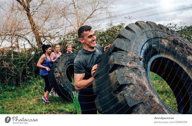 Male participant in obstacle course turning truck wheel Sports Human being Woman Adults Man Group Smiling Authentic Strong Power Effort Competition Teamwork