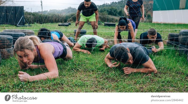 Participants in obstacle course crawling under electrified cables Sports Human being Woman Adults Man Group Meadow To enjoy Black Effort Competition Barbed wire