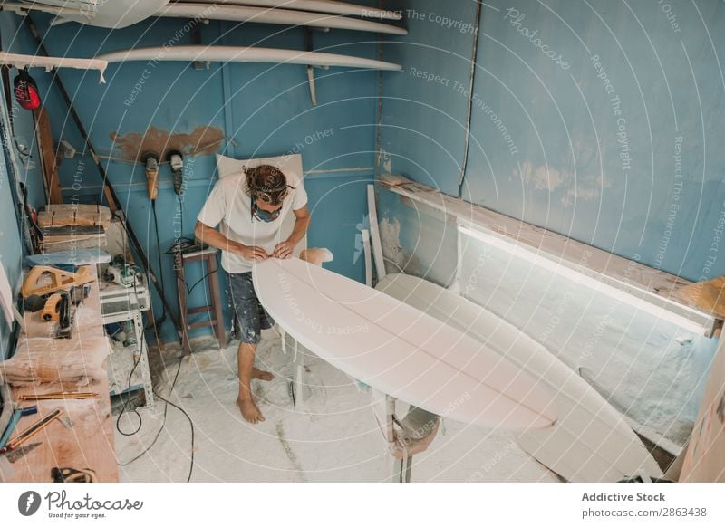 Man in respirator polishing surf board in workshop Surfboard Workshop carpentry Sandpaper Workplace Breather Carpenter Tool Weapon Wood Construction