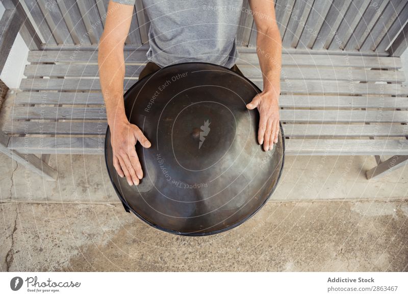 Blond man sitting on bench with big hand drum Man Drum handpan Bench Sit Hand Barefoot T-shirt Seat Blonde Window Door Building Music Guy instrument Playing