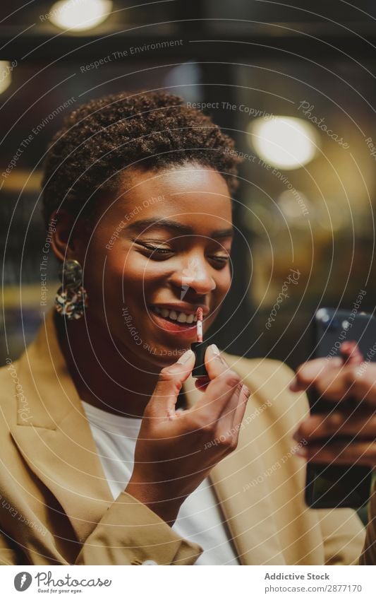 Stylish black woman rouging lips and holding smartphone on street Woman PDA Lips Street Black African-American Elegant Style Lipstick Closed eyes City Cellphone