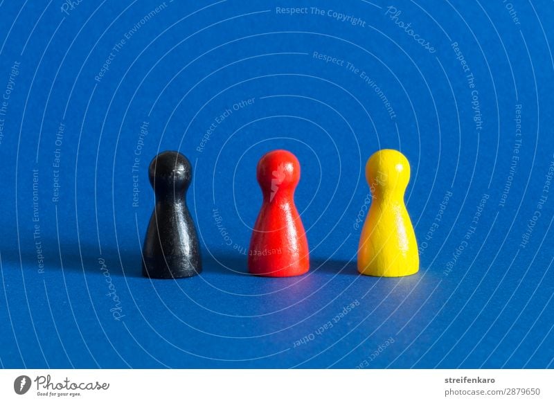 Three game pieces in black, red and yellow stand in a row on a blue background Economy Toys Wood Select Stand Blue Yellow Gold Red Black Acceptance Protection