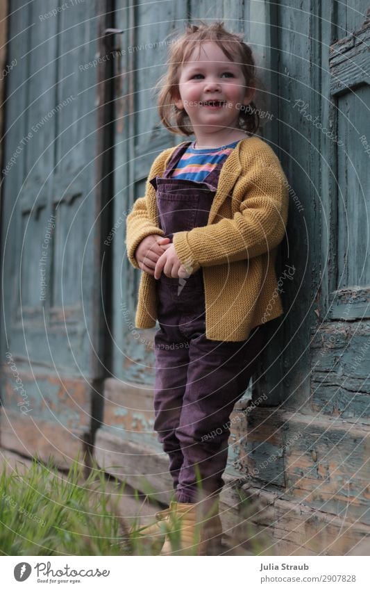 little girl standing at petrol blue old wooden gate laughing Feminine Toddler Girl 1 Human being 1 - 3 years Old town Goal door Cardigan Overalls Brunette