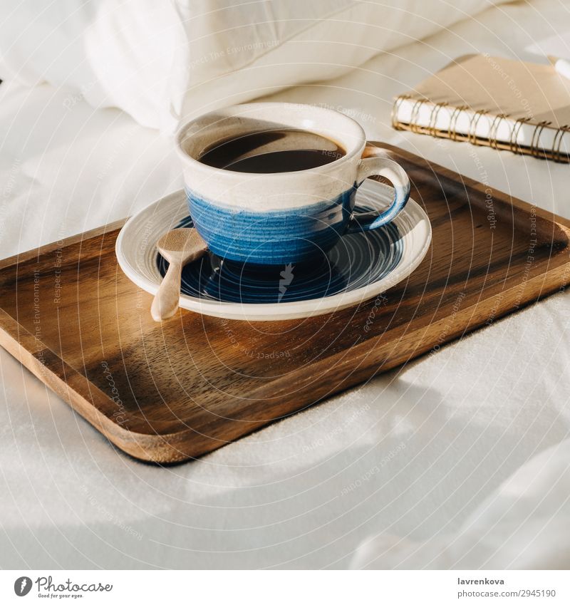 Coffee on wooden tray with notebook and pen on bed Neutral Background Bedroom Beverage Breakfast Brown Cup Hot Morning Mug Notebook Paper Pen Pillow Sheet Spoon