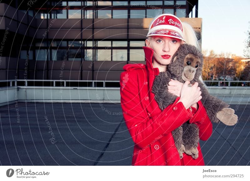 Young woman in red coat presses her cuddly toy a little monkey against her and looks into the camera.... Style Leisure and hobbies Adventure Woman Adults Life