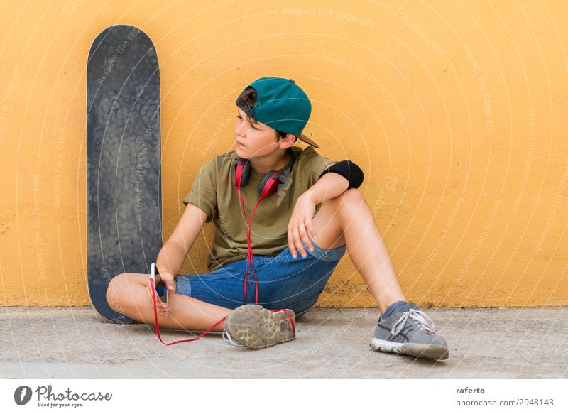 boy sitting on ground leaning on a wall while using a mobile Child Telephone PDA Technology Human being Masculine Boy (child) Youth (Young adults) 1