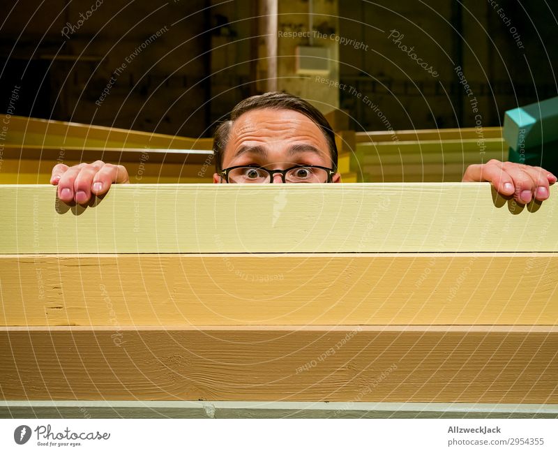 Young man looks curiously over a barrier Interior shot 1 Person Artificial light Portrait photograph Forward Looking into the camera Eyeglasses Fence Barrier