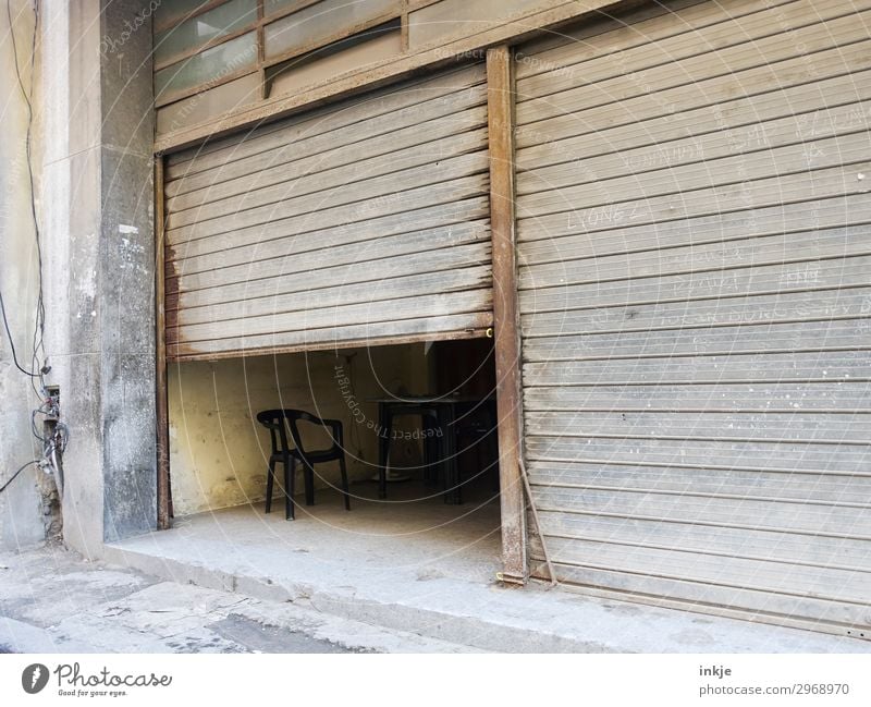 Cuban lunch break Deserted Gate Garage Garage door Disk Main gate Chair Old Authentic Dark Simple Brown Gray Half Closed Open Derelict Dusty Colour photo