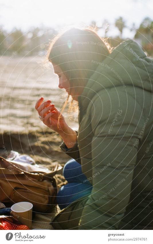 A young woman in a warm coat sitting on a ground in a park and having a small snack Leisure and hobbies Human being Young woman Youth (Young adults) Woman