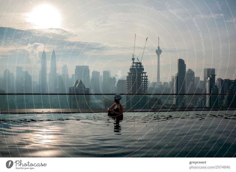 Woman enjoying cityscape of Kuala Lumpur from rooftop swimming pool. Urban scene with skyscrapers, Petronas Tower and Kuala Lumpur Tower, Malaysia Luxury