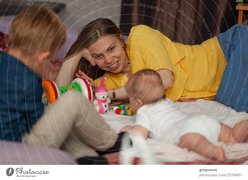 A newborn baby lying on the floor, surrounded by its toys and family - a mother and an older brother Joy Playing Human being Masculine Feminine Baby Boy (child)