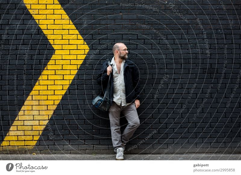 Man in front of a black wall with yellow arrows Human being Masculine Adults 1 Yellow Black Wall (building) Arrow Signs and labeling Right Left Movement