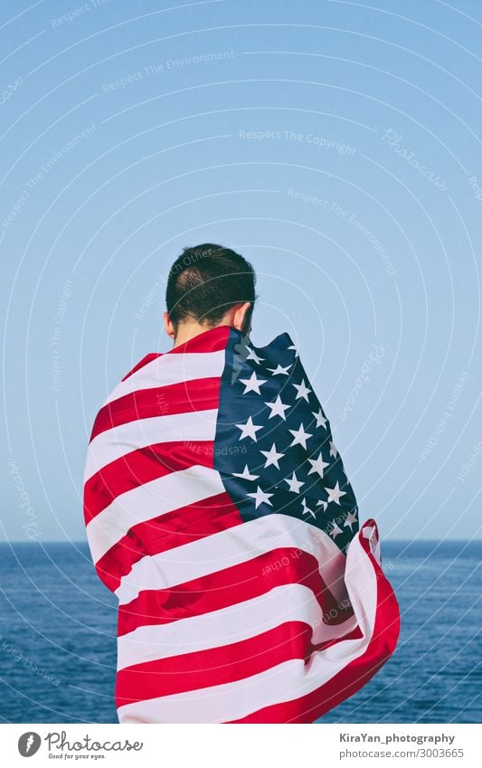 Man from behind wrapped in American Flag against blue sky Happy Freedom Ocean Feasts & Celebrations Adults Hand Sky Monument Stripe Blue Honor Independence