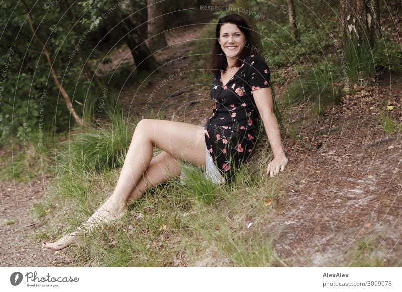 Portrait of a tall young woman sitting smiling in a clearing Lifestyle Joy luck already Young woman Youth (Young adults) Legs 18 - 30 years Adults Nature Plant