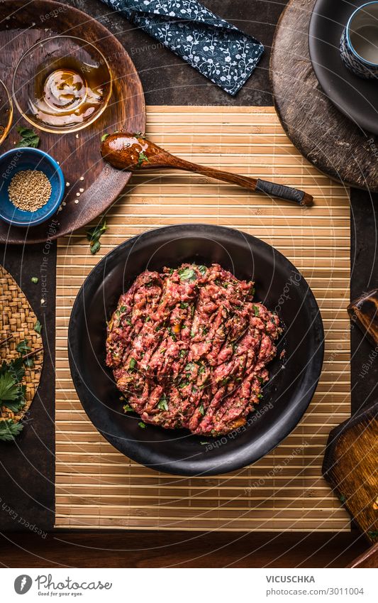 Meat stuffing in black bowl on dark rustic kitchen table with bowls and plates, top view meat concept minced meat ground meat above over recipes grinder