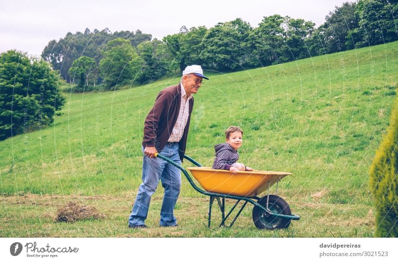 Happy senior man giving cute boy ride on wheelbarrow Lifestyle Joy Leisure and hobbies Playing Summer Garden Child Gardening Human being Boy (child) Man Adults