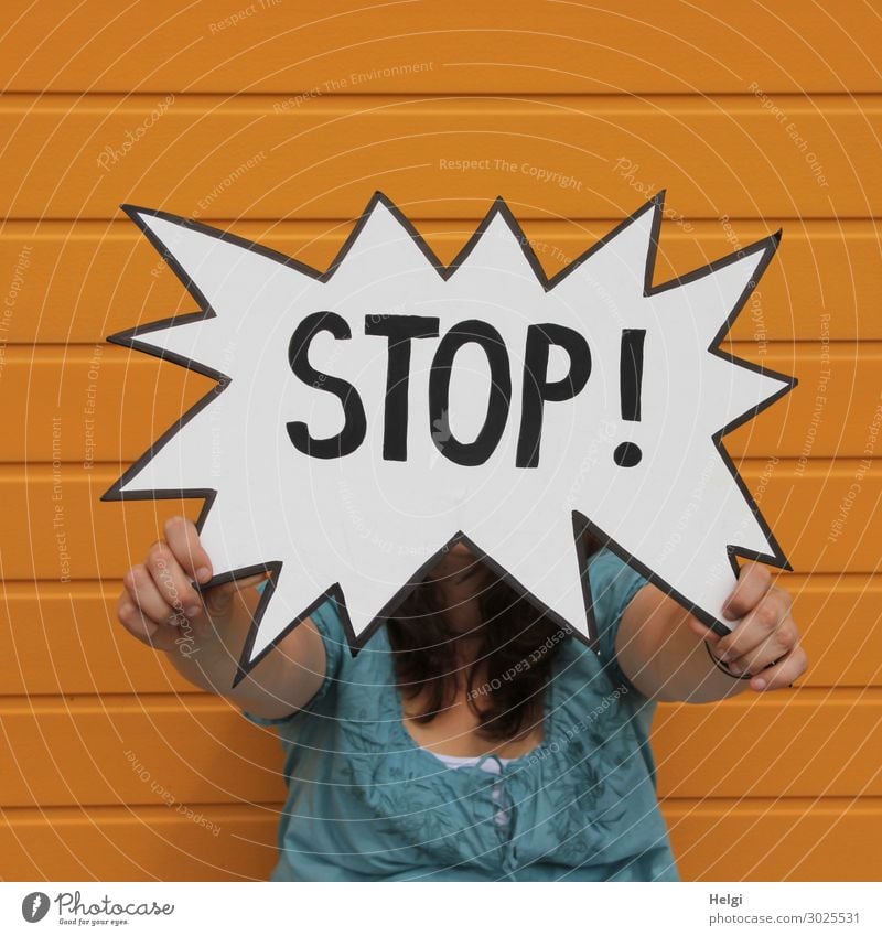 Stop sign held by a woman in front of an orange wall Hand 1 Human being 30 - 45 years Adults Facade Clothing Shirt Brunette Long-haired Characters Signage