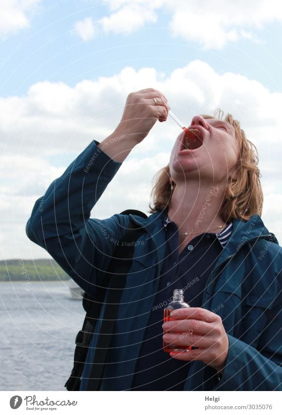 Woman with a blue jacket and long brunette hair holds her head in the neck and drips a liquid with a pipette into the wide open mouth Human being Feminine