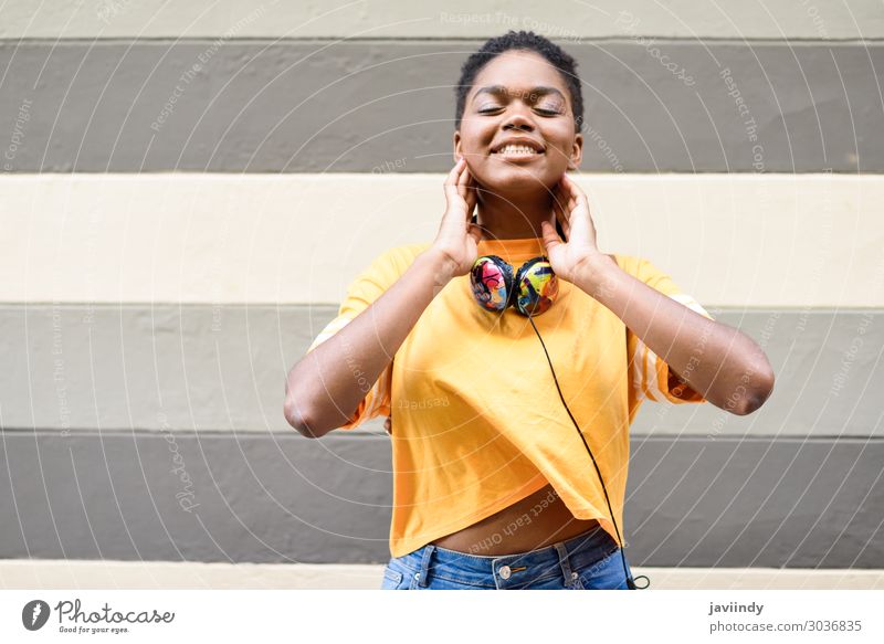 Happy African woman smiling on urban wall with eyes closed Lifestyle Style Beautiful Hair and hairstyles Face Music Headset Human being Feminine Young woman