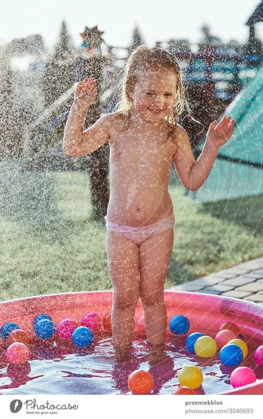 Little cute adorable girls enjoying a cool water sprayed by their father during hot summer day in backyard. Candid people, real moments, authentic situations