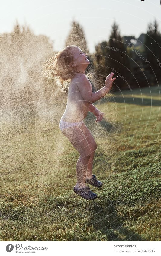 Little cute adorable girl enjoying a cool water sprayed by her mother during hot summer day in backyard. Candid people, real moments, authentic situations