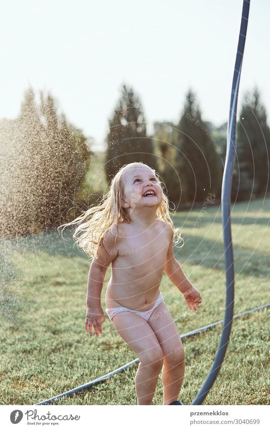 Little cute adorable girl enjoying a cool water sprayed by her mother during hot summer day in backyard. Candid people, real moments, authentic situations