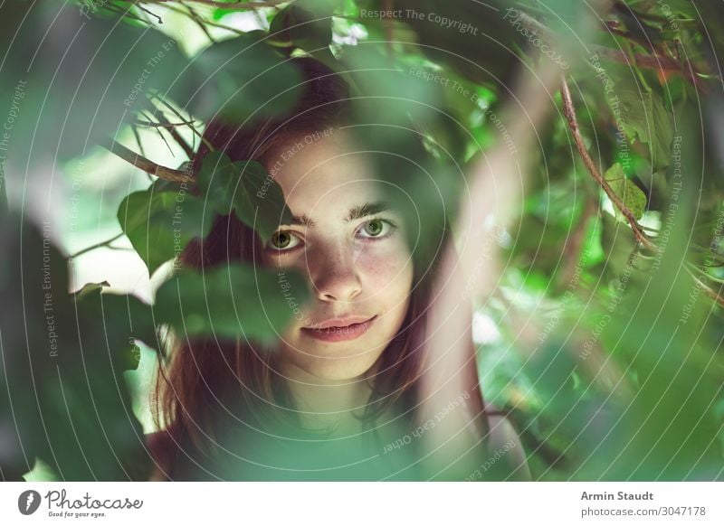 portrait of a young smiling woman covered of blurred leaves teenager girl surprise innocent authentic pure smile female candid observe beautiful tree leafs face