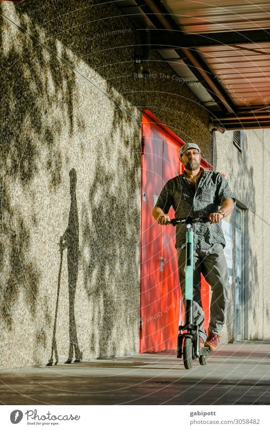 Man in cap drives electric scooter Lifestyle Shopping Trip Wall (barrier) Wall (building) Facade Transport Means of transport Traffic infrastructure Pedestrian