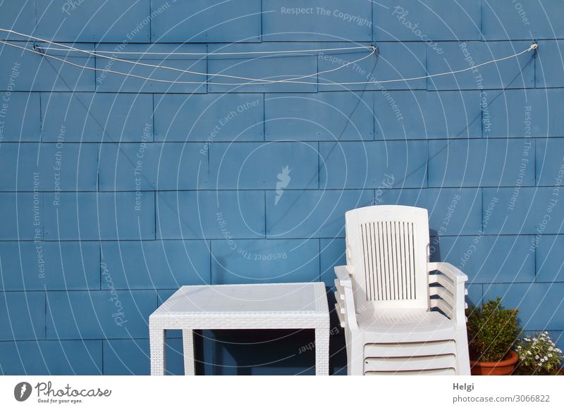 stacked white plastic chairs and a white table in front of a blue wall with clothesline Village House (Residential Structure) Wall (barrier) Wall (building)