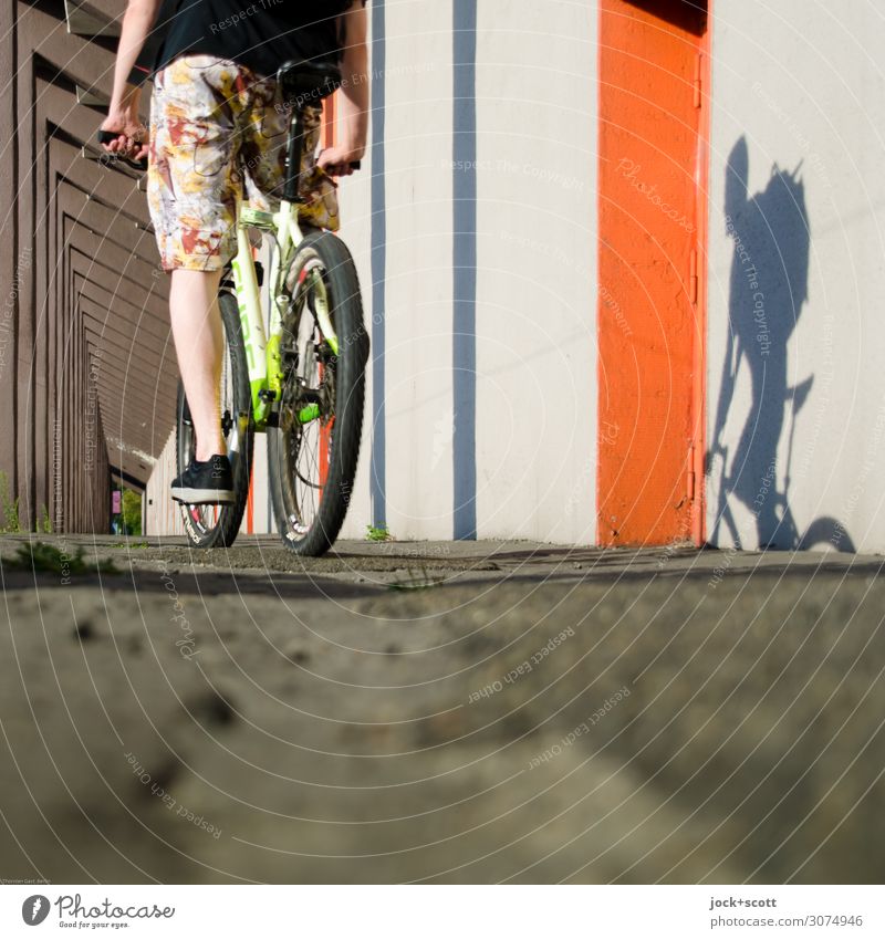 Cyclists with shadow play Cycling tour Legs Wall (building) Colonnades Ground Mountain bike Shorts Sneakers Driving Long Many Emotions Experience Mobility