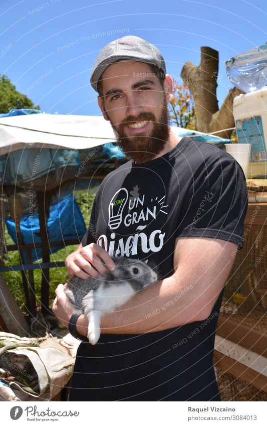 Young boy with a beard on his farm, holding a rabbit in his hands. man animal farmer beret outdoor country life Lifestyle sky