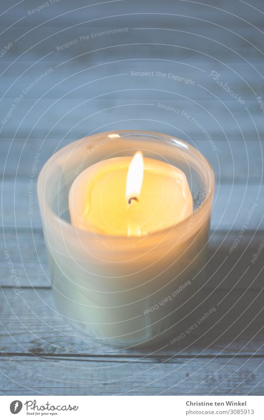 Burning candle in a candle glass on a light wooden background. Weak depth of field shoulder stand Wood Glass Illuminate Simple Bright Warmth Blue Yellow White