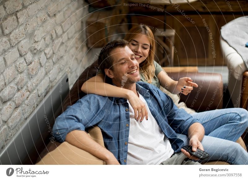 Smiling young couple relaxing and watching TV at home Lifestyle Joy Beautiful Relaxation House (Residential Structure) Sofa Technology Human being Woman Adults