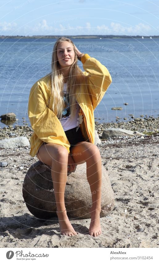 Young woman with yellow jacket on a rock on the beach Style Joy pretty Life Well-being Summer Summer vacation Sun Beach Ocean Youth (Young adults) Legs