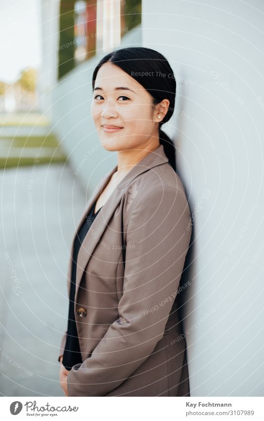 smiling asian businesswoman leaning on wall attractive beautiful beauty blazer career charming cheerful chinese confident consultant corporate dark hair