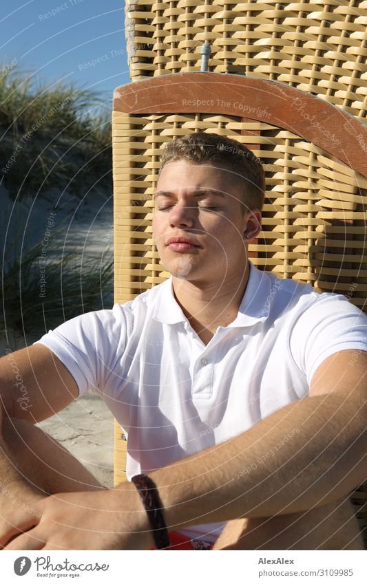 Young man sunning himself on the beach in front of a wicker beach chair Lifestyle Style Joy already Harmonious Well-being Summer Summer vacation Sun Sunbathing