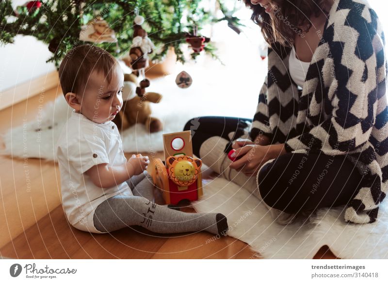 Mother and baby playing around the Christmas Tree christmas family tree mother latin hispanic happy new year child daughter holiday woman celebration mom kid