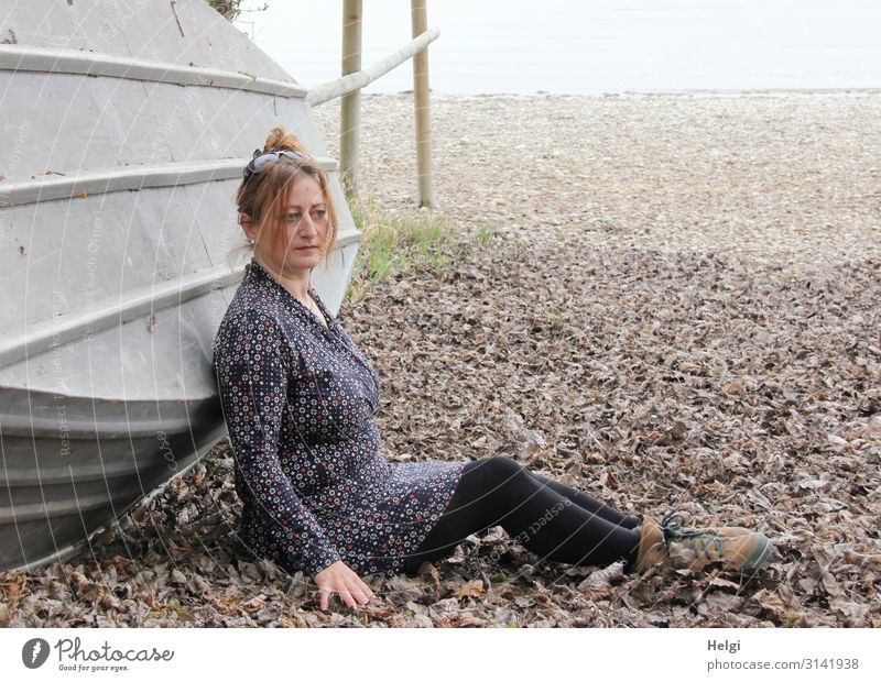 Woman with brunette hair pinned up in the leaves sitting in front of an overturned boat Human being Feminine Adults 1 45 - 60 years Environment Nature Landscape