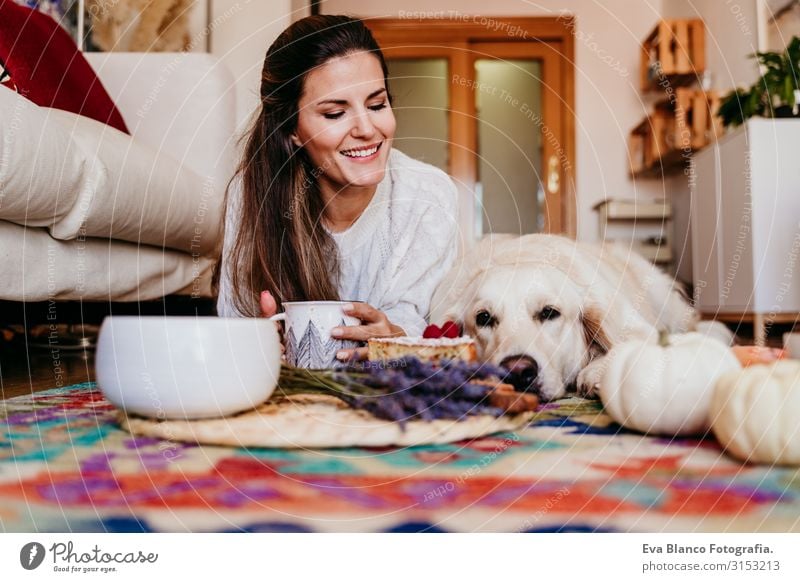 beautiful woman and cute golden retriever dog enjoying healthy breakfast at home, lying on the floor. healthy breakfast with tea, fruits and sweets. autumn season