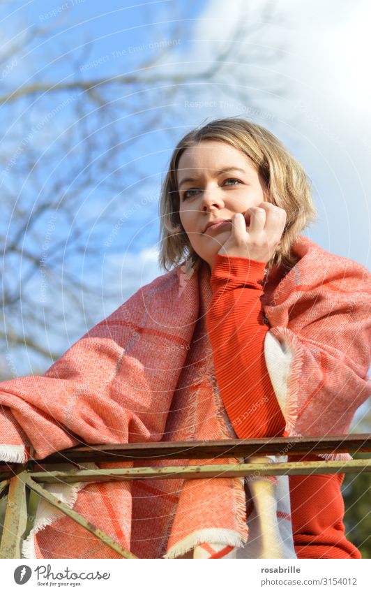 young blonde pretty woman with orange sweater and scarf is standing at the railing outside and looks thoughtfully into the distance Far-off places Human being