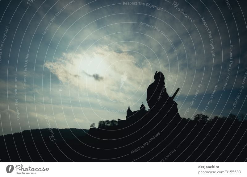 A statue as a bridge guard. With a covered sky and a backlight shot. In the background you can still see the Würzburg castle. Design Harmonious Trip Art Statue