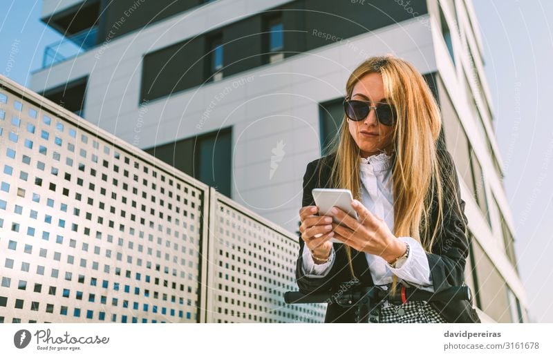 Businesswoman leaning on her electric scooter looking mobile in the street Elegant PDA Human being Woman Adults Building Street Fashion Sunglasses Blonde Modern