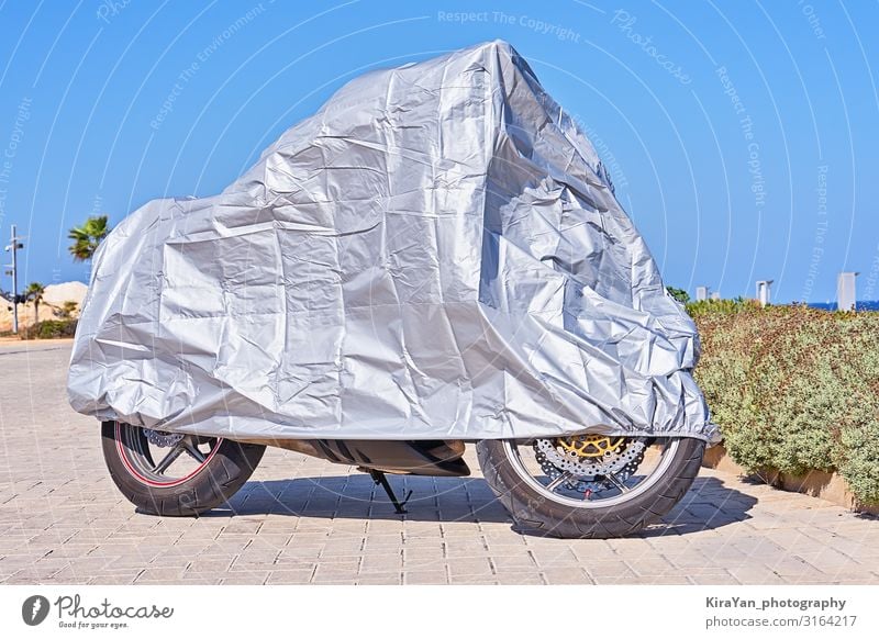 Waterproof cover for motorcycle with silver reflective protective surface. Motorcycle covered with fabric shield and parked outside Cover Blue Scooter Accessory