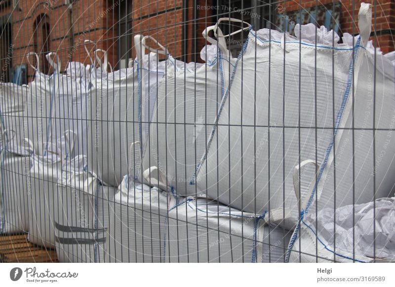 large filled white plastic bags stand on top of each other behind a building fence Hamburg Port City Wall (barrier) Wall (building) Sack Fence Stone Metal